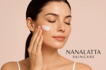 Close-up of woman applying cream to her cheek with a soft pink skincare branding background
