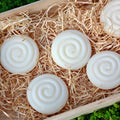 White tallow spiral-patterned soap bars on a bed of straw in a wooden box with a green grass background